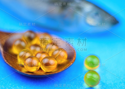 鱼油胶囊在一个棕色的木勺在蓝色的背景与鱼在背景。有选择性的重点。
