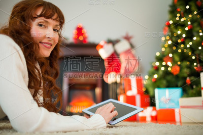 红发女人圣诞节躺在地板上用平板电脑