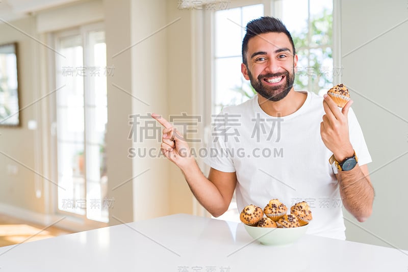 英俊的西班牙裔男子吃着巧克力片松饼非常幸福的指着用手和手指的一边