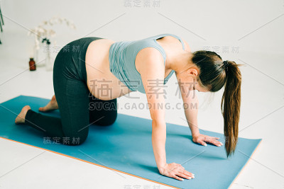 一个年轻漂亮的孕妇穿着运动服在瑜伽室的垫子上做体式
