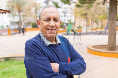 英俊的中年老人笑容开朗，幸福和积极的双臂交叉在城市城镇