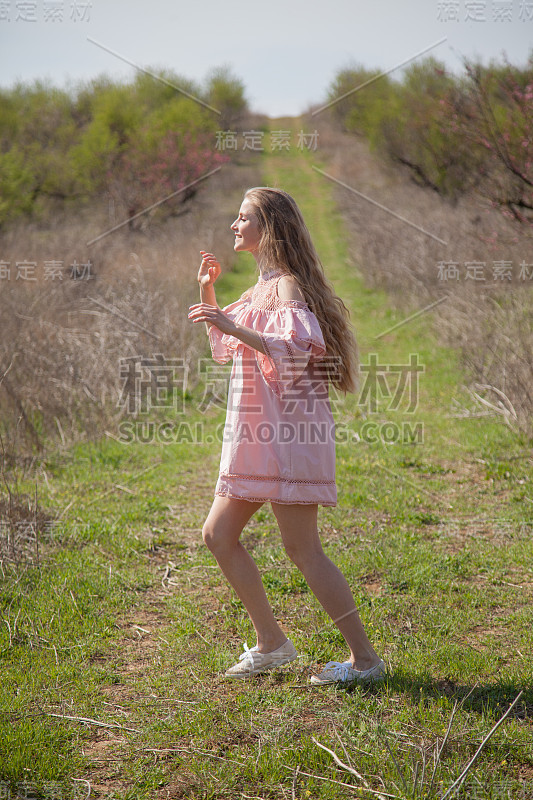 穿着粉红色裙子的金发美女走过鲜花盛开的花园