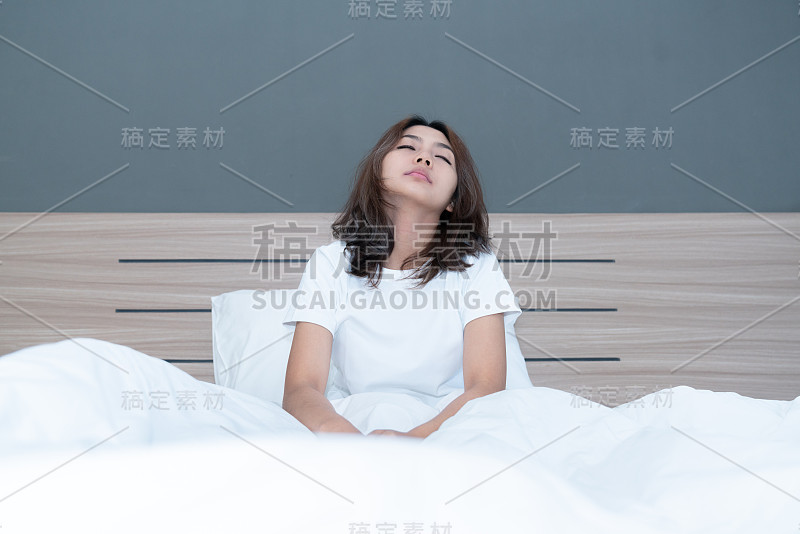 早上醒来后，年轻的亚洲女性在床上伸展和微笑。