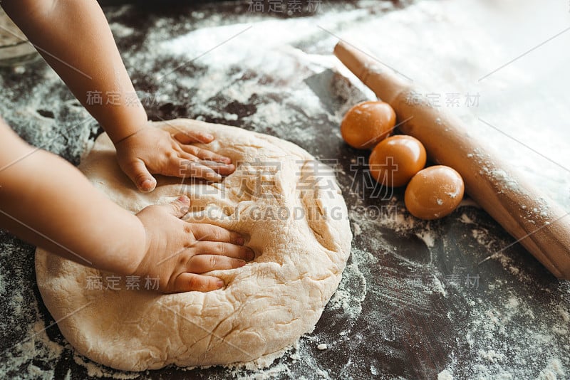 孩子的手，一些面粉，小麦面团和擀面杖放在黑色的桌子上。