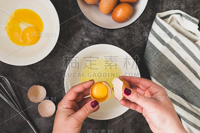 烹饪omlette。女人的手煮煎蛋卷，打破一个新鲜的鸡蛋。黑暗的背景。食物平。