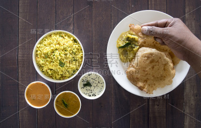 一只印度手正在采摘印度食物Poori。木桌上的印度食物俯视图