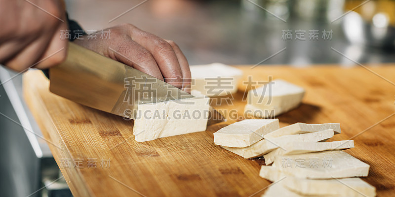 厨师之手用刀在木砧板上切豆腐奶酪