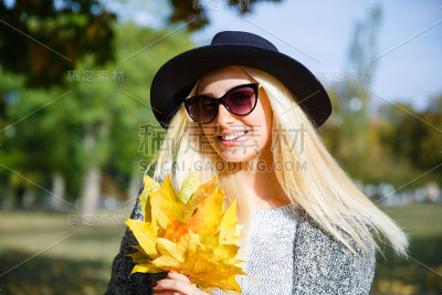 一个快乐的女孩在秋天的树叶中间的公园里散步。