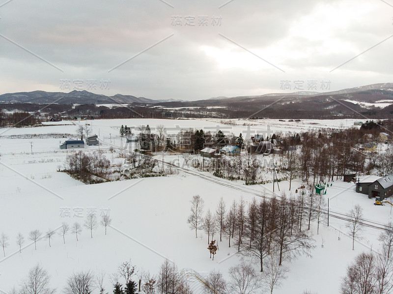 冬天的风景照片，雪覆盖的田野和村舍与光秃秃的树木在前景和雄伟的Yotei山在背景