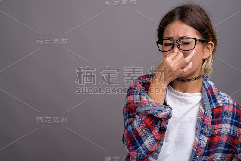 工作室拍摄的年轻亚洲妇女穿着格子衬衫，以灰色背景