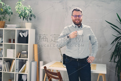 年轻的男建筑师站在现代的办公室里，手里拿着一杯咖啡。