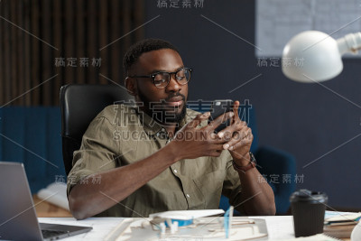 年轻的美国黑人微笑着使用智能手机。快乐的商人使用手机应用程序，发短信，浏览互联网，看智能手机。使用移