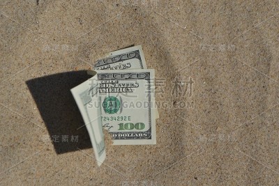 钱美元一半覆盖着沙子躺在海滩上特写。
