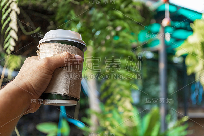 特写男性的手拿着一个热咖啡杯与软焦点和在背景过光