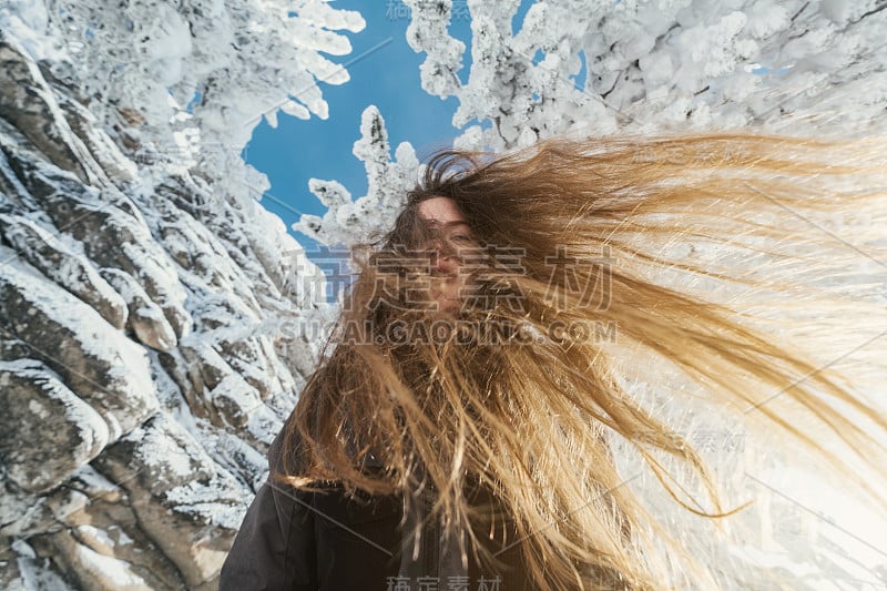 美丽的冬日画像下的年轻女子，白雪覆盖的杉树和悬崖，漂亮的微笑，长长的头发，阳光灿烂的冬日