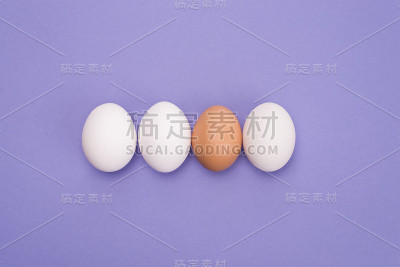 领导的概念。上面是三个鸡蛋的近景照片和一个鸡蛋的棕色壳孤立在紫色的背景