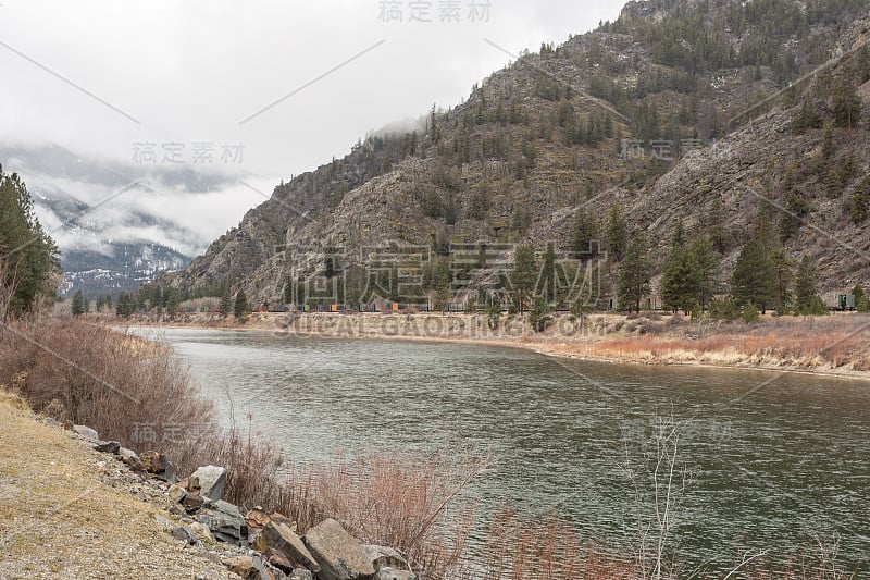 空的火车车厢休息在树木覆盖的山和平静的河旁边