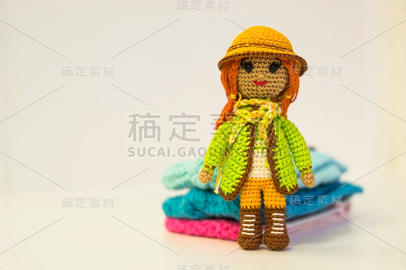 编织的娃娃女孩戴着一顶帽子和编织的彩色衣服-彩色的amigurumi玩具在一个光的背景。副本的空间。