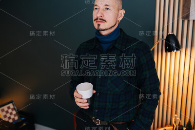 骄傲严肃的中年男子拿着一个杯子，在家里喝着热饮。
