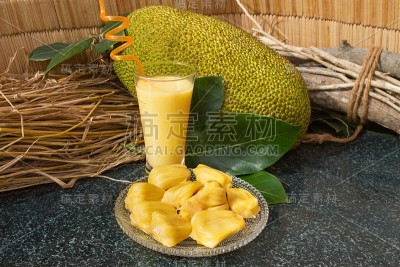 玻璃杯里的菠萝蜜汁。新鲜甜美的菠萝蜜切片放在玻璃盘子里。