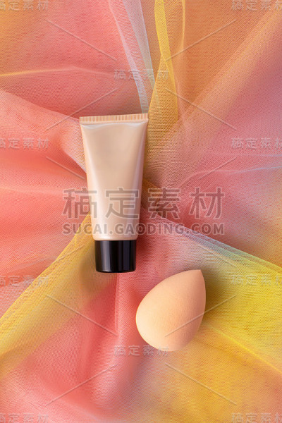 模拟色调CC或BB霜粉底化妆和美容海绵在彩色彩虹欧根纱织物上搅拌。化妆品