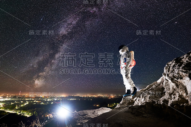 宇航员站在岩石山丘上，在奇异的星空下。