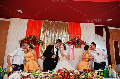 新婚夫妇和伴郎与伴娘在桌边接吻。