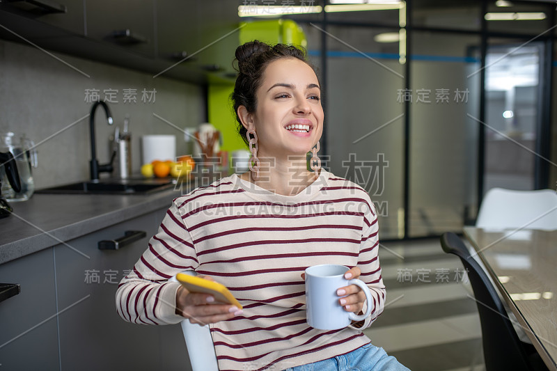 年轻女子拿着杯子和电话，微笑着