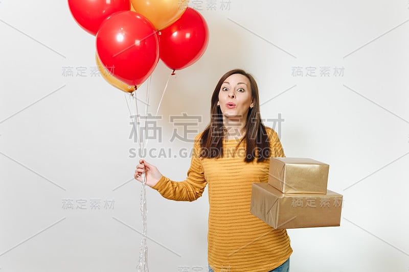 美丽的白人有趣的年轻幸福的女人在黄色的衣服，拿着生日红气球，金色的礼盒与礼物，庆祝节日派对上的白色背