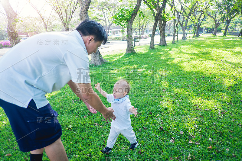 1岁亚洲小孩的第一步，快乐的宝宝和爸爸在自然中学习走路