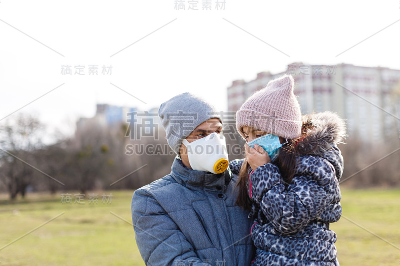 在流感流行或空气污染时，父亲和女儿在寒冷的天气要穿得暖和，并戴上防护口罩。一个男人和一个孩子在城市的