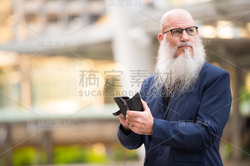 成熟的秃头商人在城市户外使用电话时思考