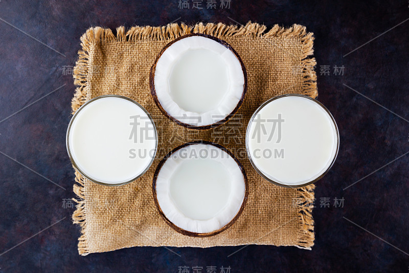 深色背景上的椰奶和玻璃椰子。椰子纯牛奶，非奶制品，麻布。健康饮料的概念。替代牛奶。平躺