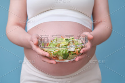 一名孕妇手里拿着一碗沙拉，背景是蓝色的