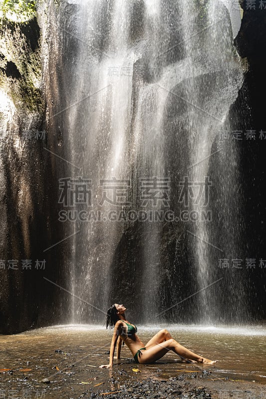 高兴的黑发女孩坐在瀑布下