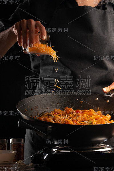 厨师将意大利面与蔬菜和肉类放在煎锅中煎炸，并加入冷冻马苏里拉芝士。在黑色的背景上。烹饪和食谱书。美味