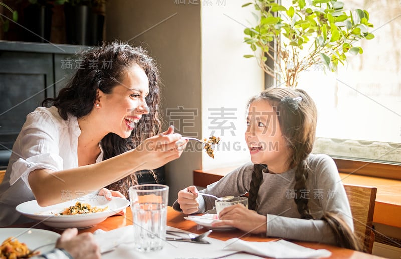 拉丁妈妈和女儿一起在餐厅吃午饭，多民族家庭玩得很开心