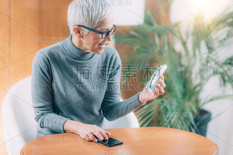 妇女使用智能手机应用程序，用非接触式数字体温计记录体温