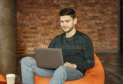 一个坐在豆袋椅上拿着笔记本电脑的人在工作空间里工作
