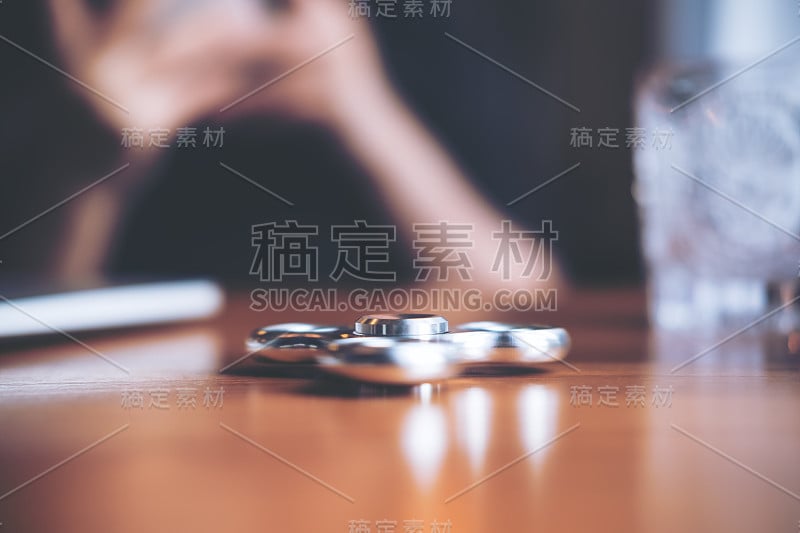 一个金属的银色指尖陀螺放在木桌上，背景是一个人