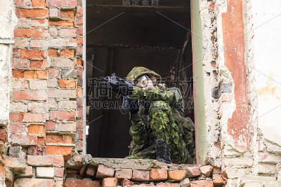 身着迷彩服的武装女子的肖像。年轻的女兵用枪观察。儿童兵与枪在战争壁炉，房子废墟的背景。军民观念，军民