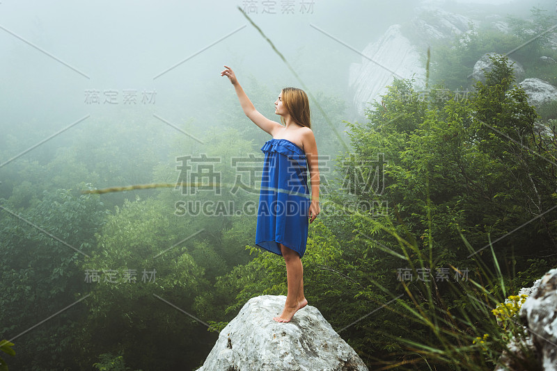 在雾霾天气中，在山中穿着蓝色连衣裙摆姿势的女性