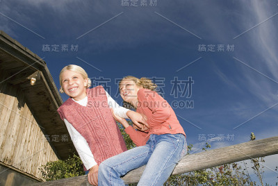 两个女孩坐在木栏杆上