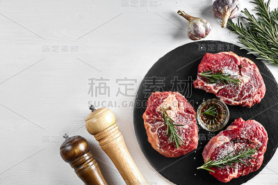 新鲜的生牛排配香草，大蒜，橄榄油，胡椒，盐和迷迭香在黑板上:里脊肉，Striploin，肋眼