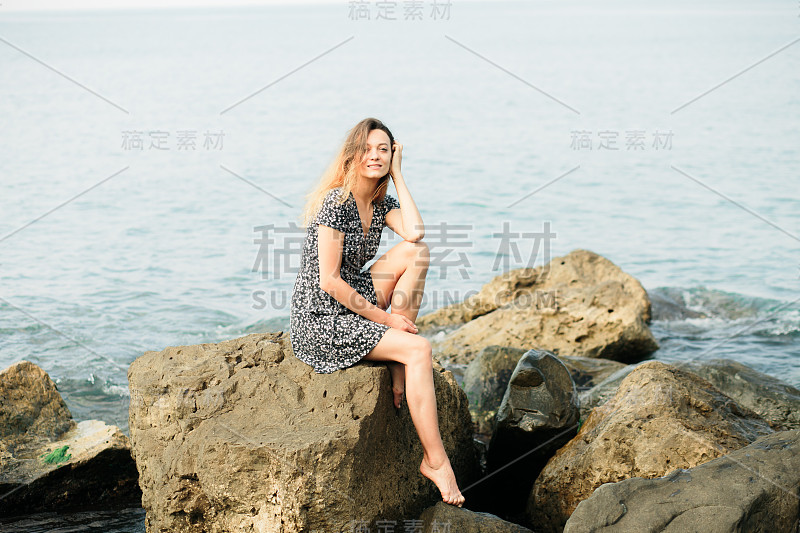 一个年轻美丽的女孩穿着大石头，风景如画的海边