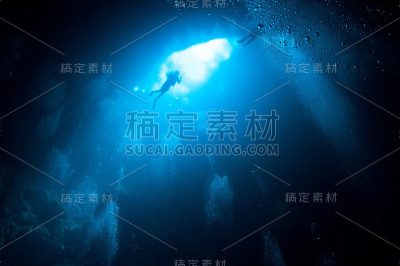 潜水员从下面带着气泡靠近蓝色明亮的坑入口