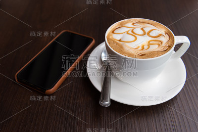 热拿铁艺术咖啡杯和手机放在木桌上