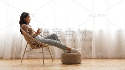完全放松。坐在扶手椅上享受咖啡的女孩