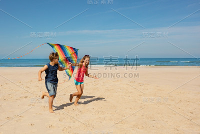 两个男孩和女孩带着彩色风筝在海滩上奔跑