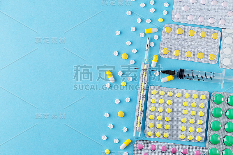 不同的药片、医用水银温度计和蓝色背景的注射器。